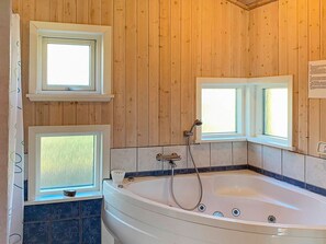 A bathroom with a large bathtub, wooden walls, and two windows. - Holiday Home in Gilleleje (Gilleleje)