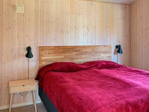 A room with a wooden headboard bed, a small bedside table, and a wall-mounted lamp. - Holiday Home in Gilleleje (Gilleleje)
