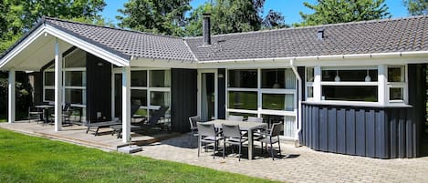 Une maison moderne dotée d’un patio couvert, de grandes fenêtres et d’un chemin en briques.
