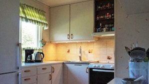 Une cuisine avec des meubles blancs, une cuisinière, un évier et une fenêtre ornée d’un rideau vert.