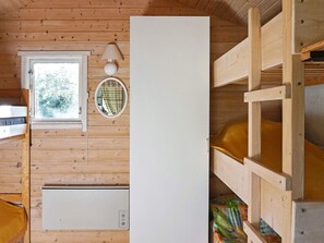 L'intérieur d'une cabane en bois, avec un lit superposé, une fenêtre donnant sur un paysage agréable, une lampe fixée au mur et un meuble blanc.