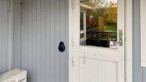 Une porte blanche avec une fenêtre, une boîte aux lettres et un petit espace extérieur délimité par une clôture.