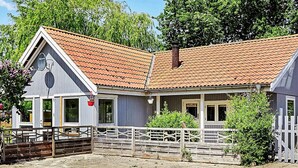Un bâtiment avec un toit en tuiles, une clôture en bois et une zone pavée devant.