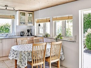 A kitchen with wooden cabinets, a dining table with chairs, and a window with plants. - 4 Person Holiday Home in Store Fuglede (Store Fuglede)
