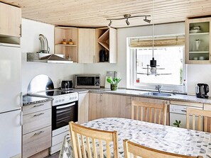 A compact kitchen with a stove, microwave, sink, and wooden cabinets. - 4 Person Holiday Home in Store Fuglede (Store Fuglede)
