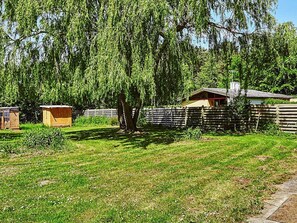 A backyard with a wooden fence, a shed, and a tree. - 4 Person Holiday Home in Store Fuglede (Store Fuglede)