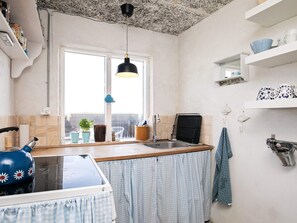 A kitchen with a window, a sink, a kettle, and a blue teapot.