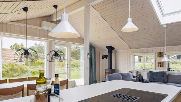 A modern kitchen with a central island, pendant lights, and a view of the outdoors. - 4 Star Holiday Home in Lokken (Lokken)
