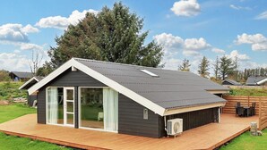 A modern house with a sloped roof, large sliding glass doors, and a wooden deck. - 4 Star Holiday Home in Lokken (Lokken)