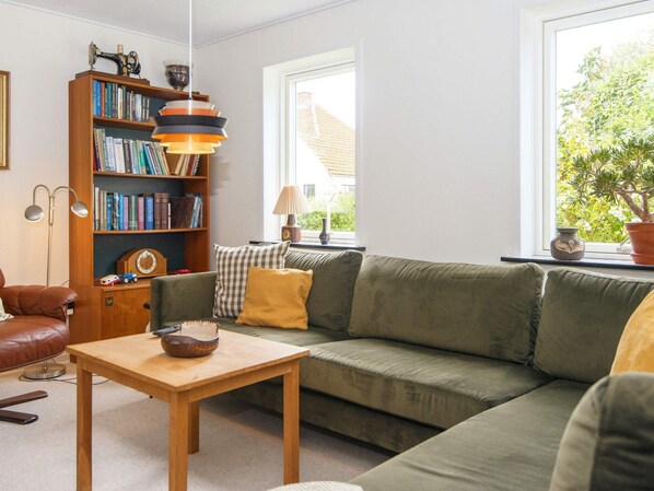 Relax in this inviting living room with a sofa, coffee table, and bookshelf, offering a peaceful view of the surrounding greenery.