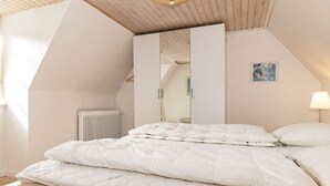 A bedroom with a sloped ceiling, a bed with white bedding, a radiator, a mirror, and a wall-mounted lamp. - Holiday Home in Marstal (Marstal)