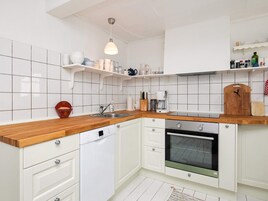 Una cocina con armarios blancos, encimera de madera, lavavajillas Bosch, cafetera y tabla de cortar de madera.