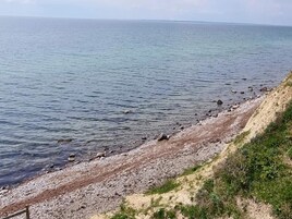 Un paisaje costero con una playa de piedras y un acantilado cubierto de hierba.
