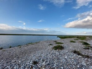 A pebbly beach with a calm body of water and a clear sky.