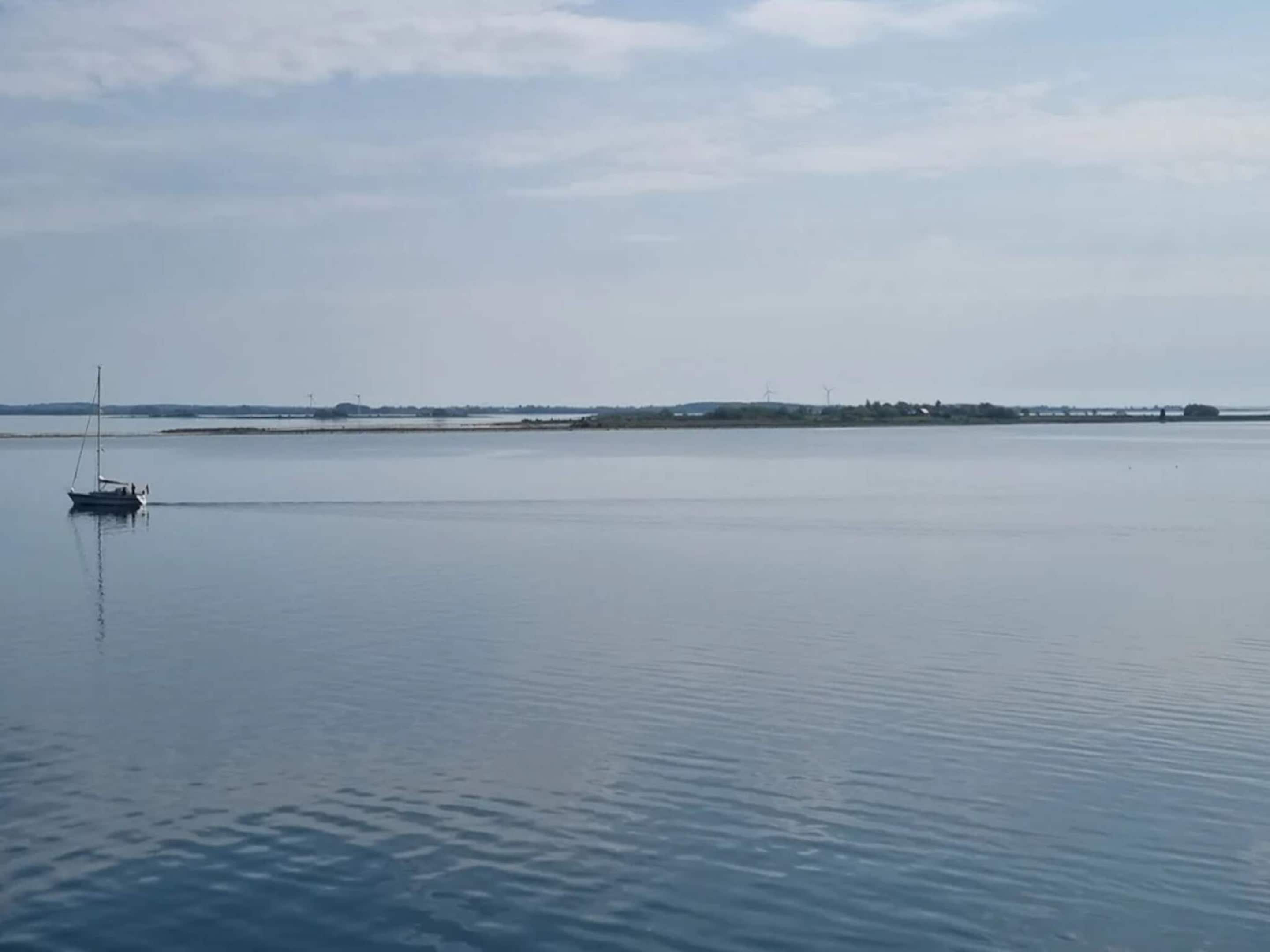 A calm body of water with a single sailboat anchored near the shore.