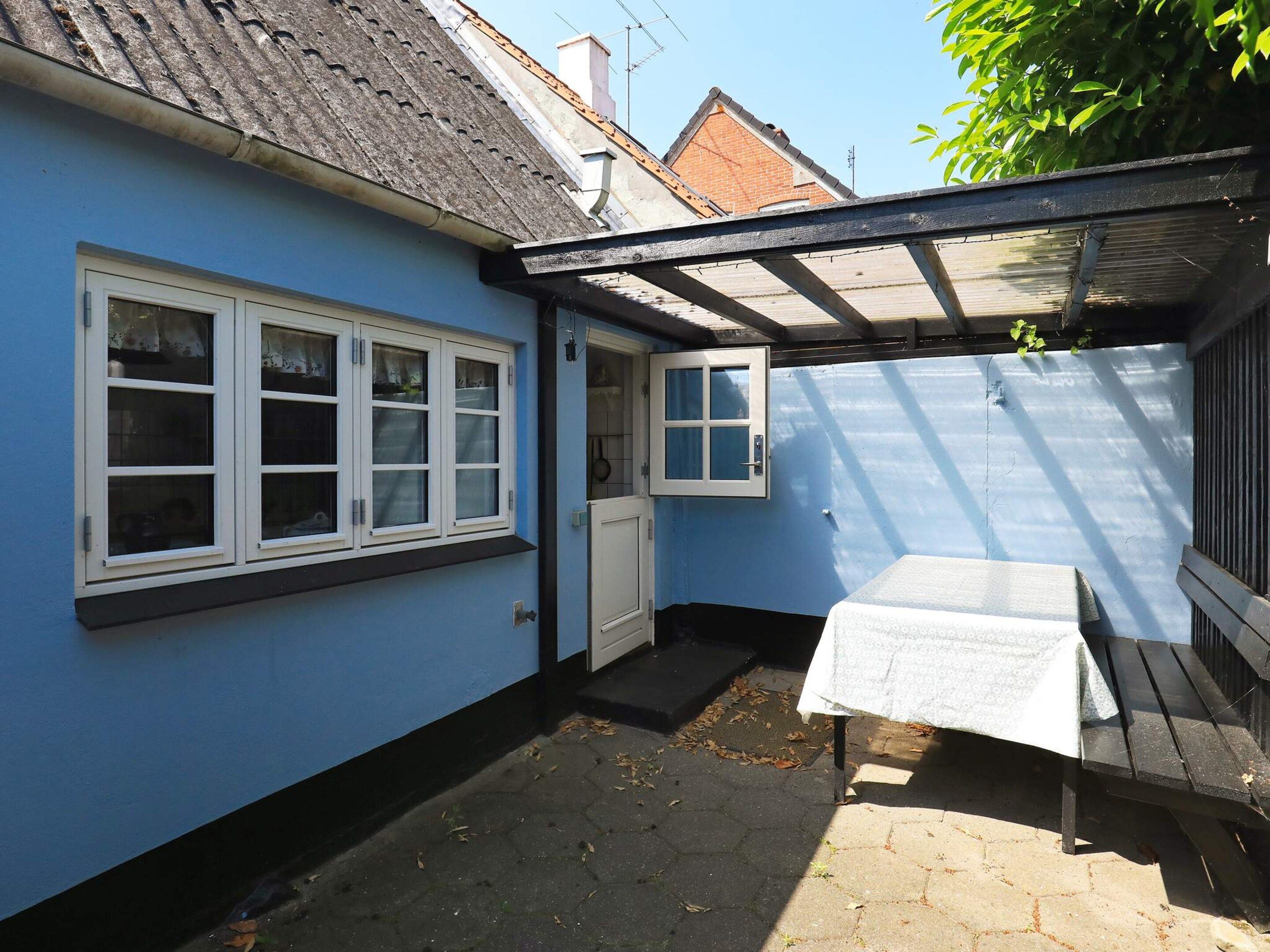A blue exterior wall with a door and windows, a covered patio area with a table, and a tiled floor.