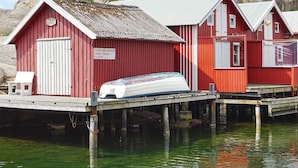A row of red wooden buildings with white doors, a white boat on a dock, and calm water. - 4 Person Holiday Home in Smogen (Smogen)
