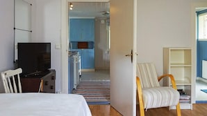 A room with a bed, a TV, a chair, a bookshelf, and a kitchen area in the background. - 4 Person Holiday Home in Smogen (Smogen)