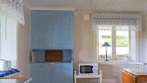 A room with a blue cabinet, a microwave on a cart, a table with a chair, and a window with lace curtains. - 4 Person Holiday Home in Smogen (Smogen)