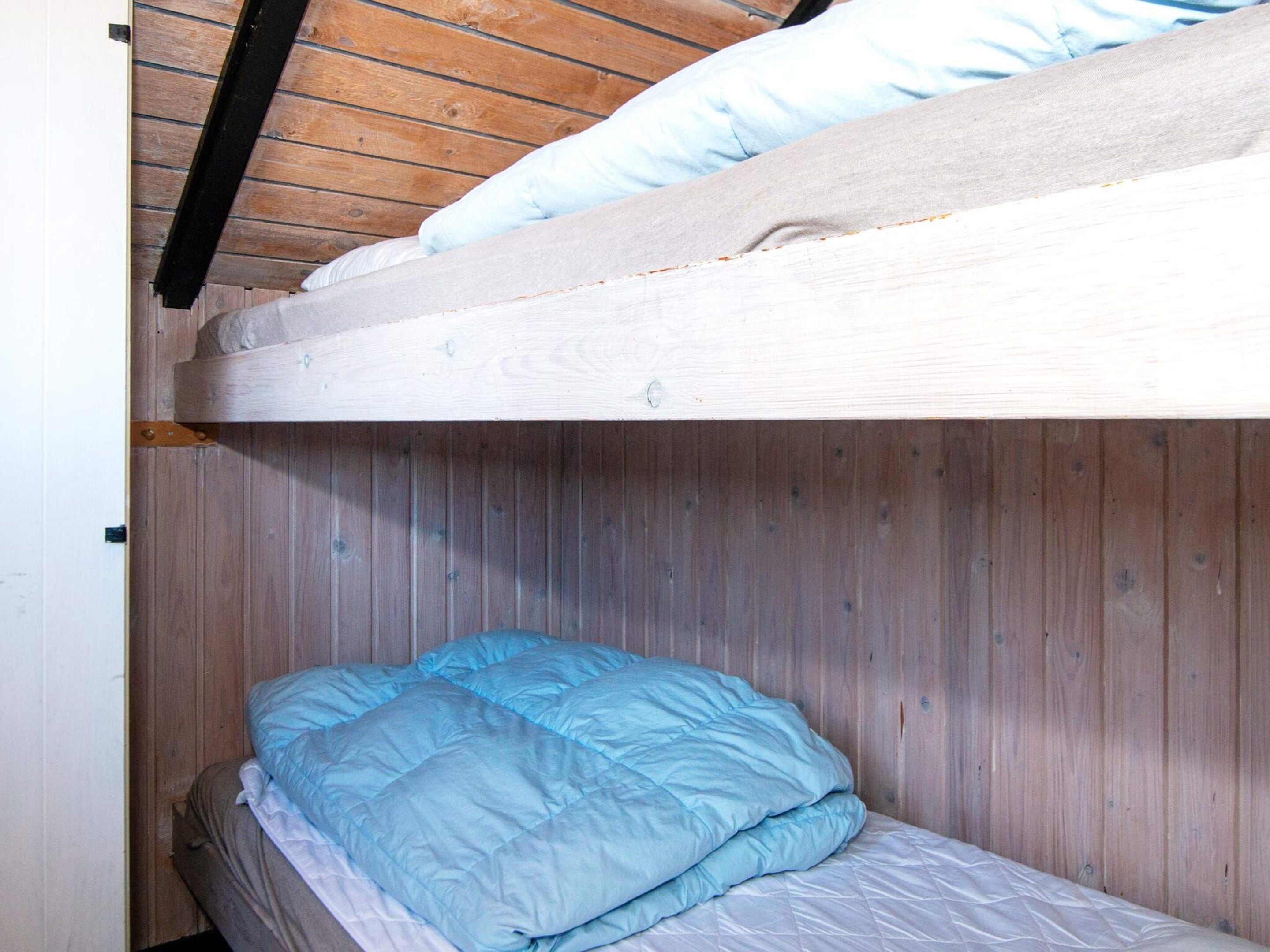En køjeseng med blå madras og puder, trævægge og et skråt loft.
