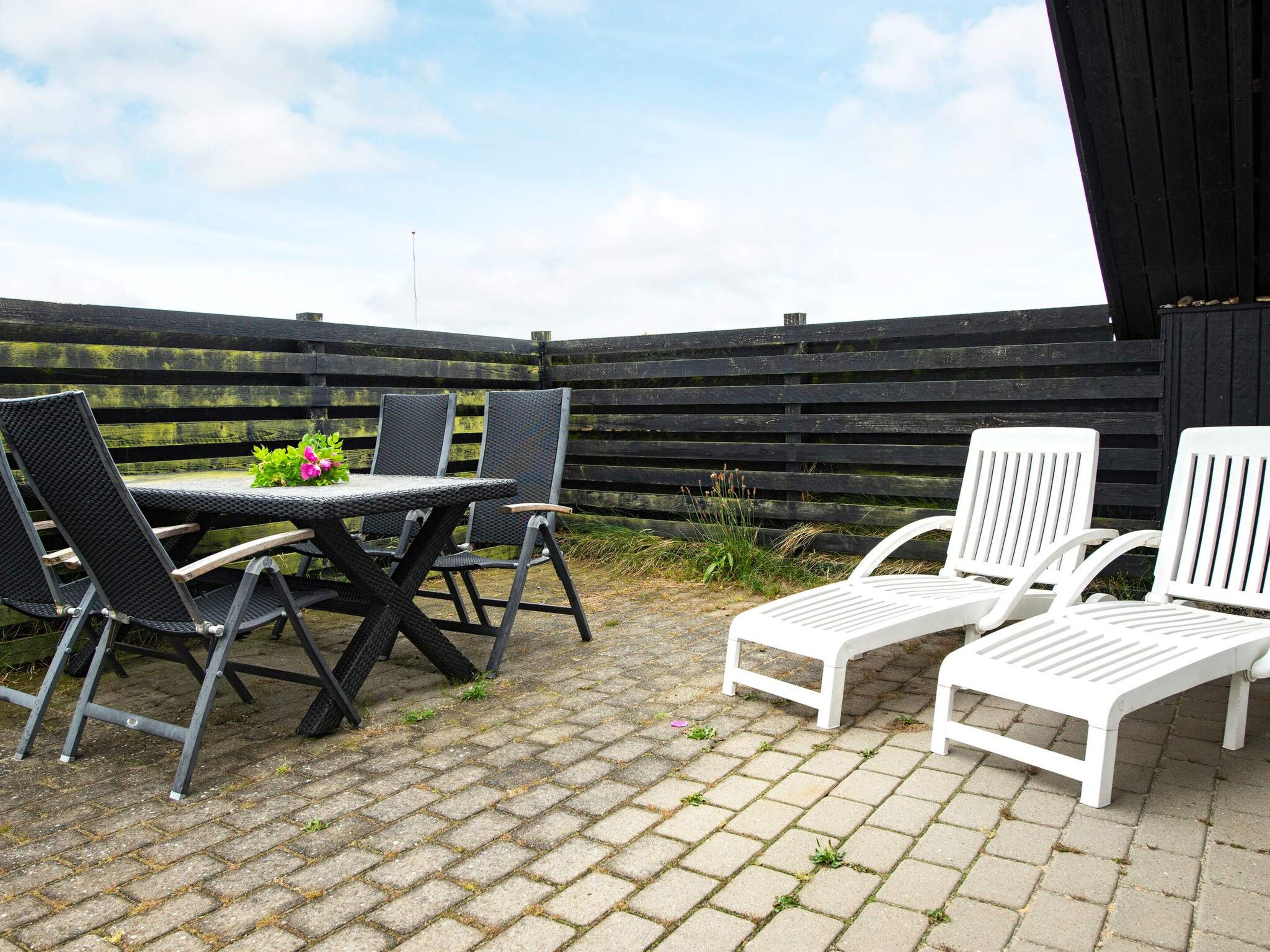 Une terrasse extérieure avec une table et des chaises, une clôture en bois en arrière-plan et un ciel dégagé.