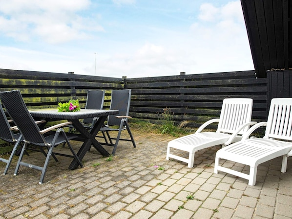 An outdoor patio with a table and chairs, a wooden fence in the background, and a clear sky.