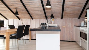 A modern kitchen with a wooden ceiling, a central island, black chairs, and a dining table. - 4 Person Holiday Home in Hvide Sande (Hvide Sande)