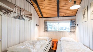 Une chambre avec deux lits, des murs en bois, une fenêtre avec des rideaux et un luminaire suspendu.