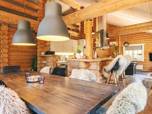 A rustic cabin interior with a wooden dining table, two pendant lights, a kitchen area, and a cozy seating arrangement. - Holiday Home in VÃ¦ggerlÃ¸se (Vaeggerlose)