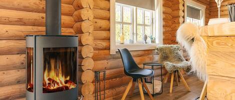 Interno di una baita in legno con stufa a legna, pareti di legno, una finestra e una poltrona.
