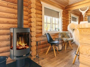 A log cabin interior with a wood-burning stove, wooden walls, a window, and a chair. - Holiday Home in VÃ¦ggerlÃ¸se (Vaeggerlose)