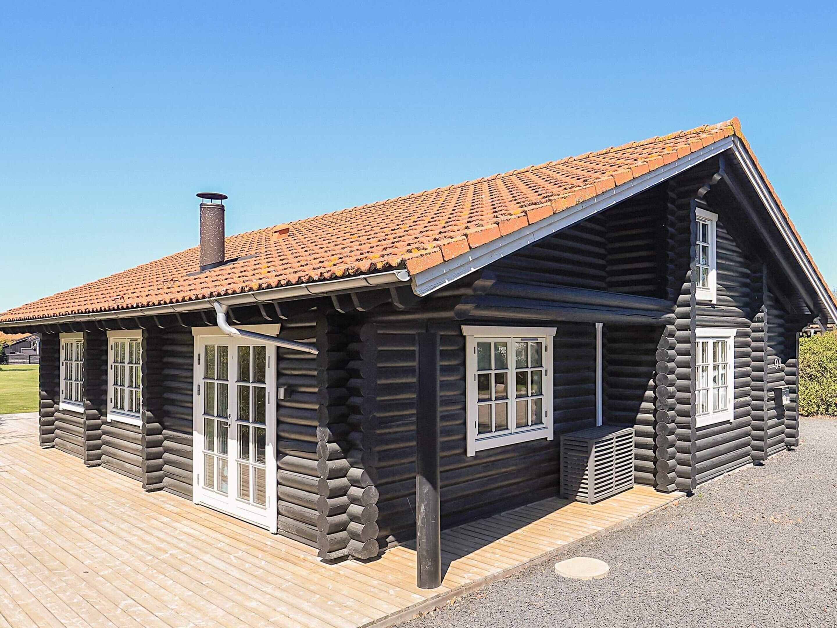Een vakantiehuisje van hout met pannendak, schoorsteen en een houten terras.