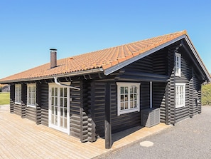 A log cabin with a tiled roof, a chimney, and a wooden deck. - Holiday Home in VÃ¦ggerlÃ¸se (Vaeggerlose)