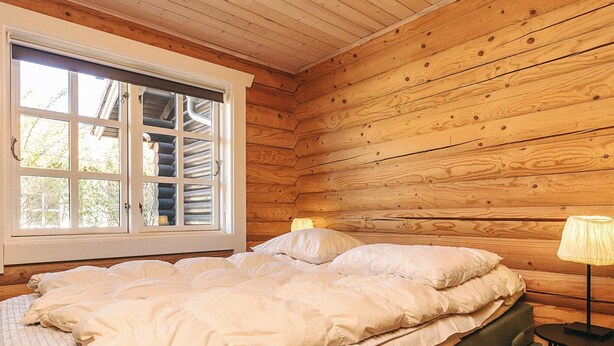 Une pièce aux murs lambrissés, avec un lit, une fenêtre et une lampe.