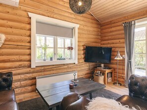 L’intérieur d’une cabane en rondins, avec un téléviseur, une table, des canapés en cuir et une fenêtre décorée de fleurs.
