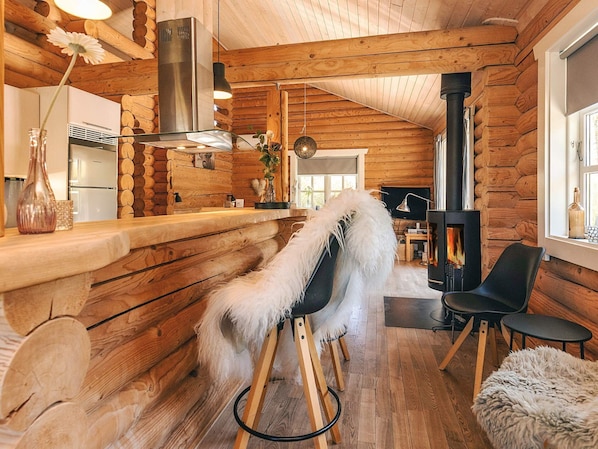 A log cabin interior with a wooden bar, a fireplace, a dining area, and a cozy seating arrangement.