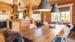 Un vaste espace dédié à la salle à manger, avec une table et des chaises en bois, une cuisine dotée de poutres apparentes en bois et de grandes fenêtres.