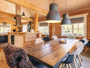 Un vaste espace dédié à la salle à manger, avec une table et des chaises en bois, une cuisine dotée de poutres apparentes en bois et de grandes fenêtres.