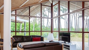 A spacious room with a large window, a sofa, a table, and a television. - Holiday Home in Gedser (Gedser)