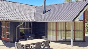 A modern house with a tiled roof, a wooden deck, and a glass-enclosed patio area. - Holiday Home in Gedser (Gedser)