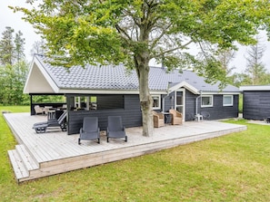 A modern house with a deck, outdoor seating, and a large tree.