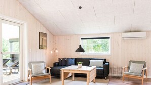 A cozy living room with a wooden floor, a dark sofa, two armchairs, a coffee table, and a large window with a view of greenery. - 6 Person Holiday Home in Henne (Henne)