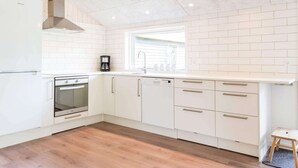 A modern kitchen with white cabinetry, a built-in oven, a coffee maker, and a window with blinds. - 6 Person Holiday Home in Henne (Henne)