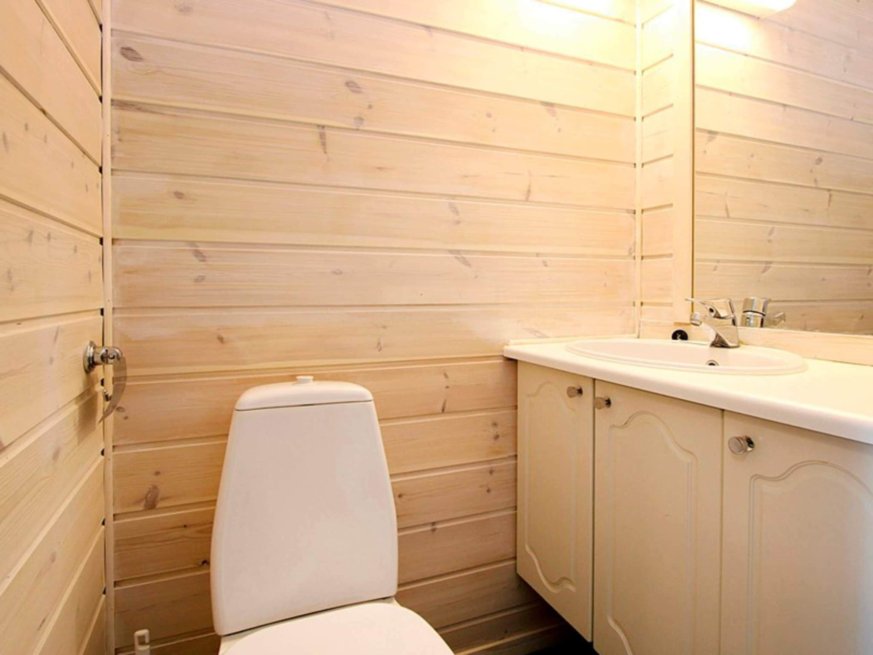 Un baño pequeño con paneles de madera, un inodoro, un lavamanos y un espejo.