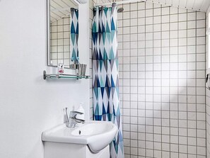 A bathroom with a white sink, a mirror, a shower curtain, and a tiled wall.
