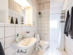 Een badkamer met een witte wastafel, toilet en spiegel. Handdoeken hangen aan de muur en een plant hangt aan het plafond.