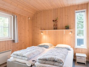 A room with wooden walls, a bed with multiple pillows, a bedside table, and a shelf with plants. - 4 Star Holiday Home in Norre Nebel (Norre Nebel)