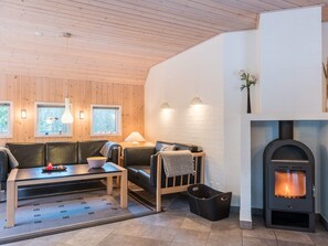 A cozy living room with a fireplace, wooden walls, and a sofa. - 4 Star Holiday Home in Norre Nebel (Norre Nebel)
