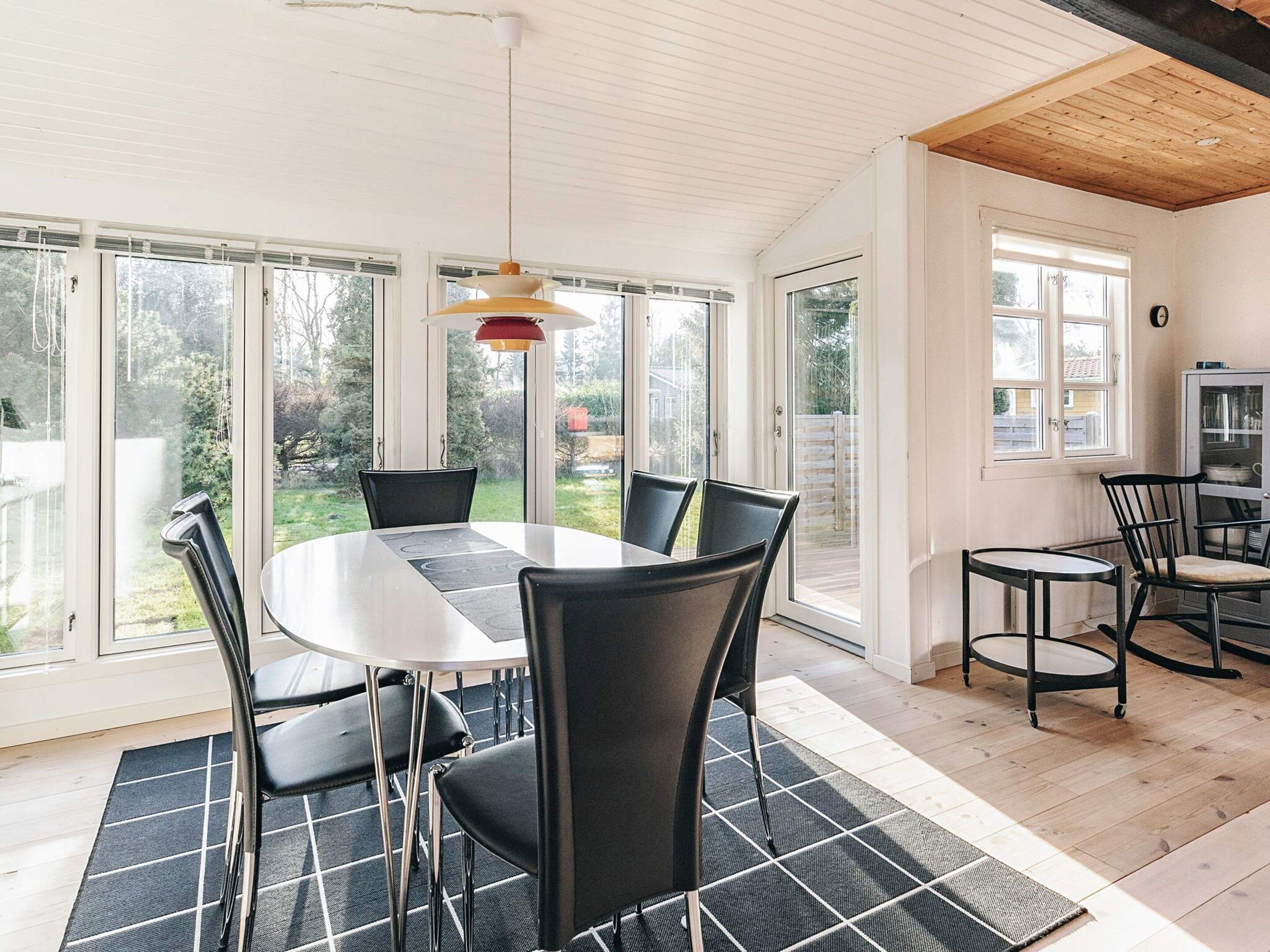 A dining area with a round table and chairs, large windows, and a ceiling with exposed beams.