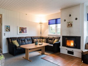 A cozy living room with a fireplace, a sofa set, a wooden coffee table, and a window with blinds.